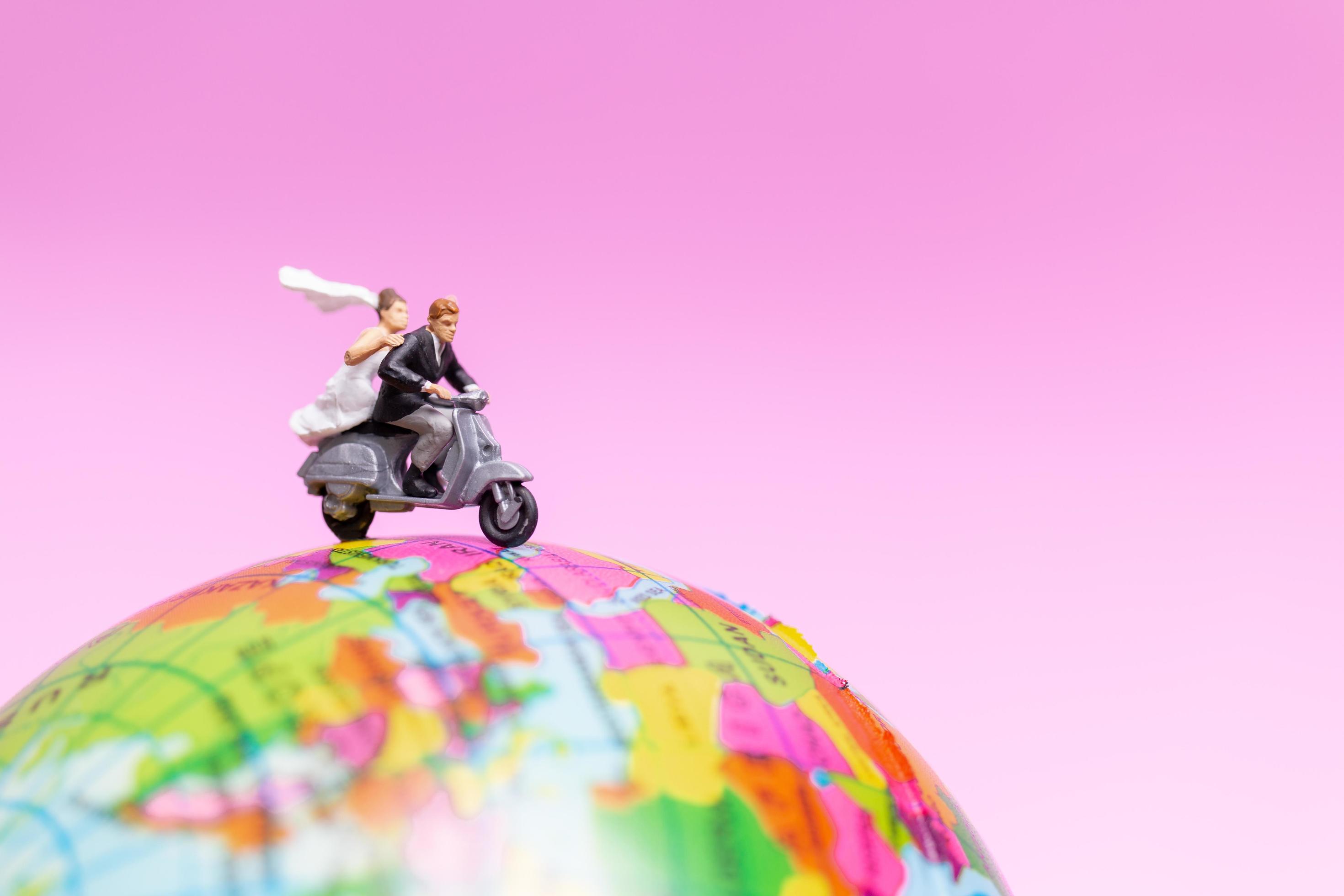 Miniature couple riding a motorcycle on a world globe Stock Free