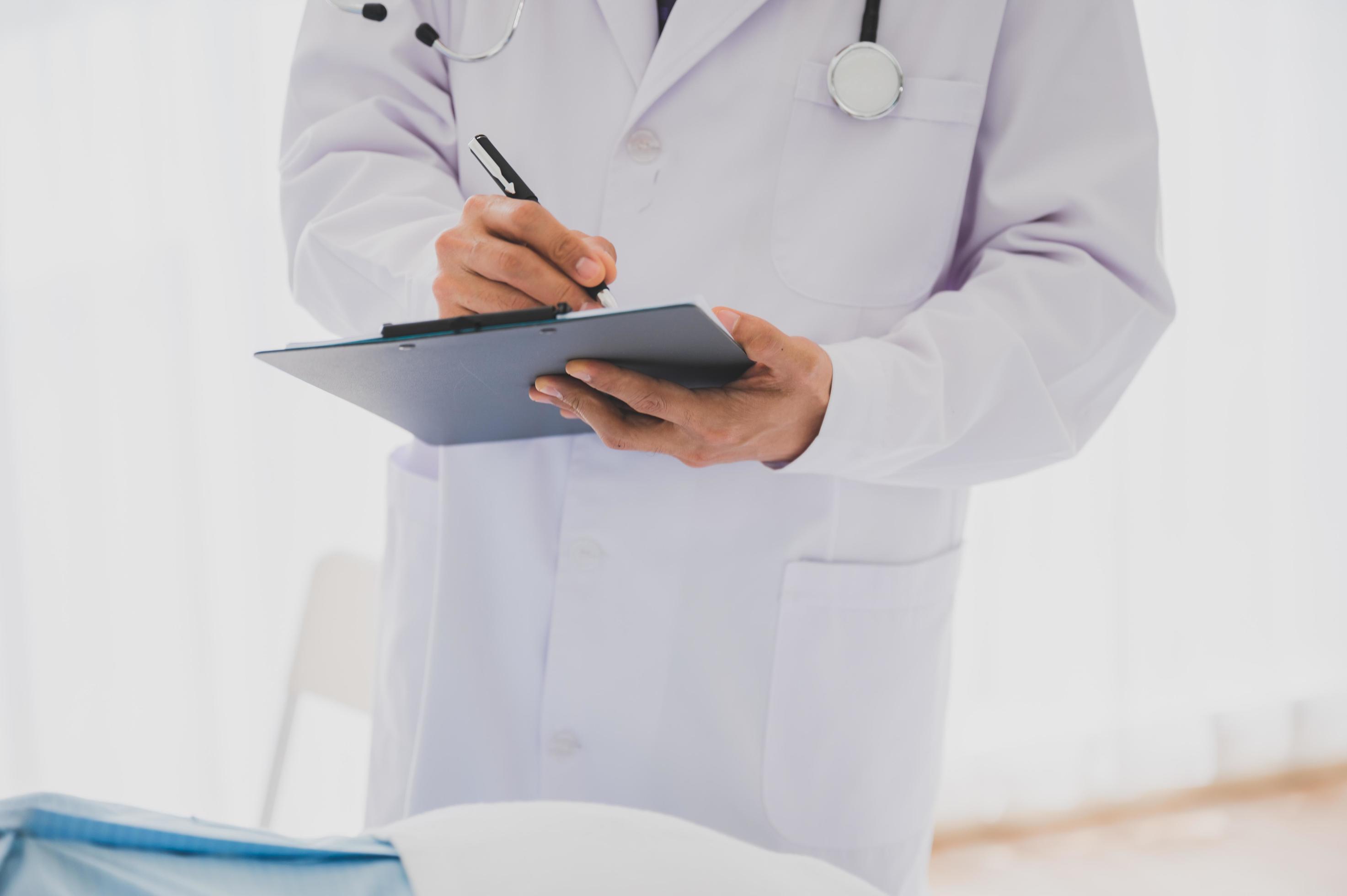 Male doctor with lab coat and stethoscope holding clipboard and pen Stock Free