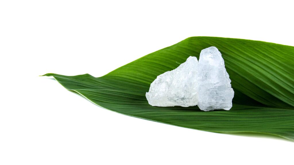 White crystal clear alum cube on green leaf isolated on white background. Stock Free