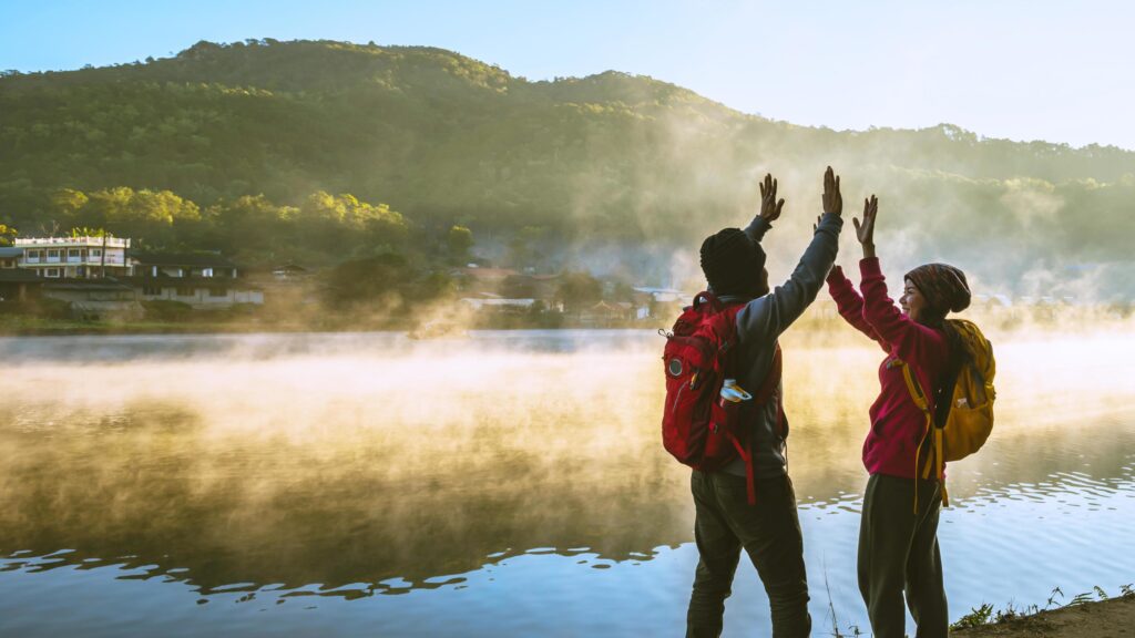 Asian woman and Asian man which backpacking standing near the lake, she was smiling, happy and enjoying the natural beauty of the mist. Stock Free