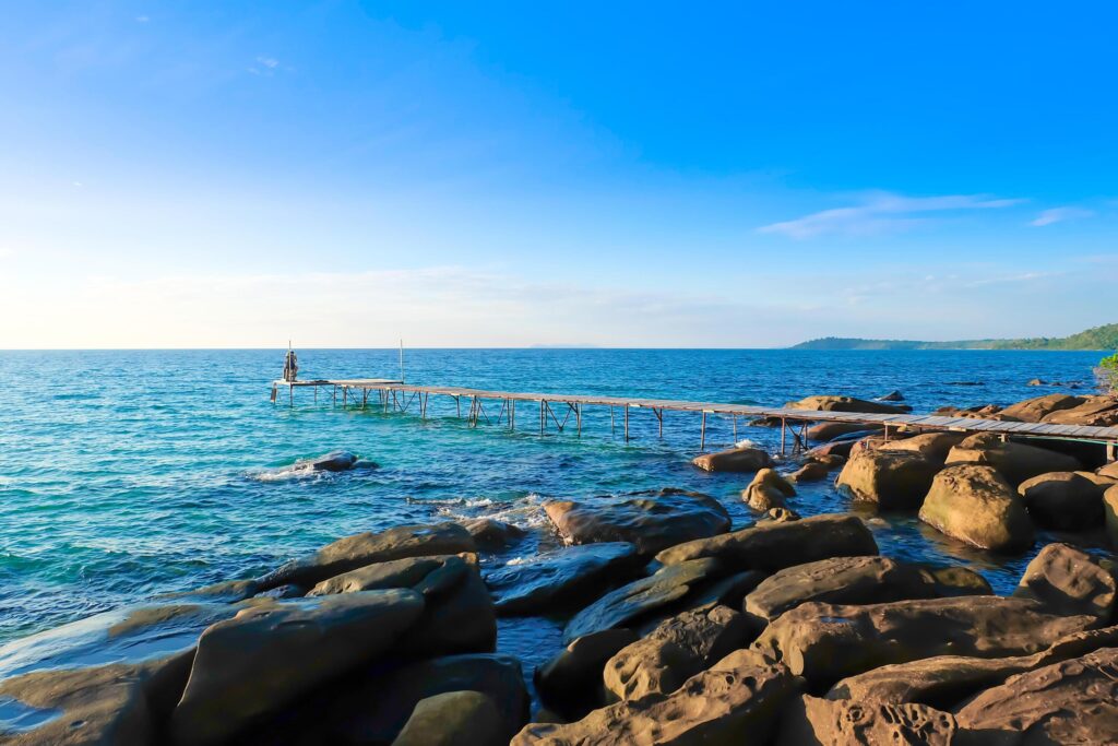 Wooden pier extended to the sea with rocky coast. sky and cloud natural background on vacation and relax time. Stock Free