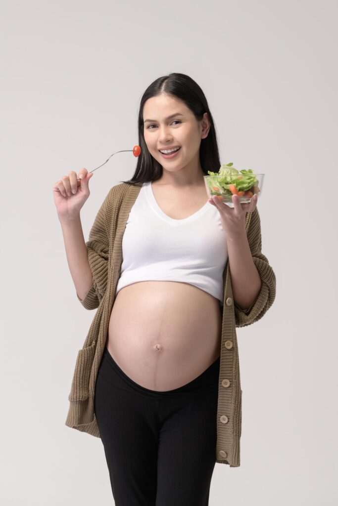 Portrait of Beautiful pregnant woman eating salad over white background studio, health and maternity concept Stock Free