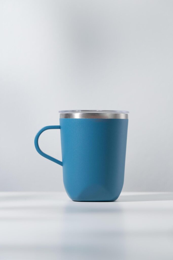 Blue tumbler made of stainless steel on a wooden table and white background. Stock Free