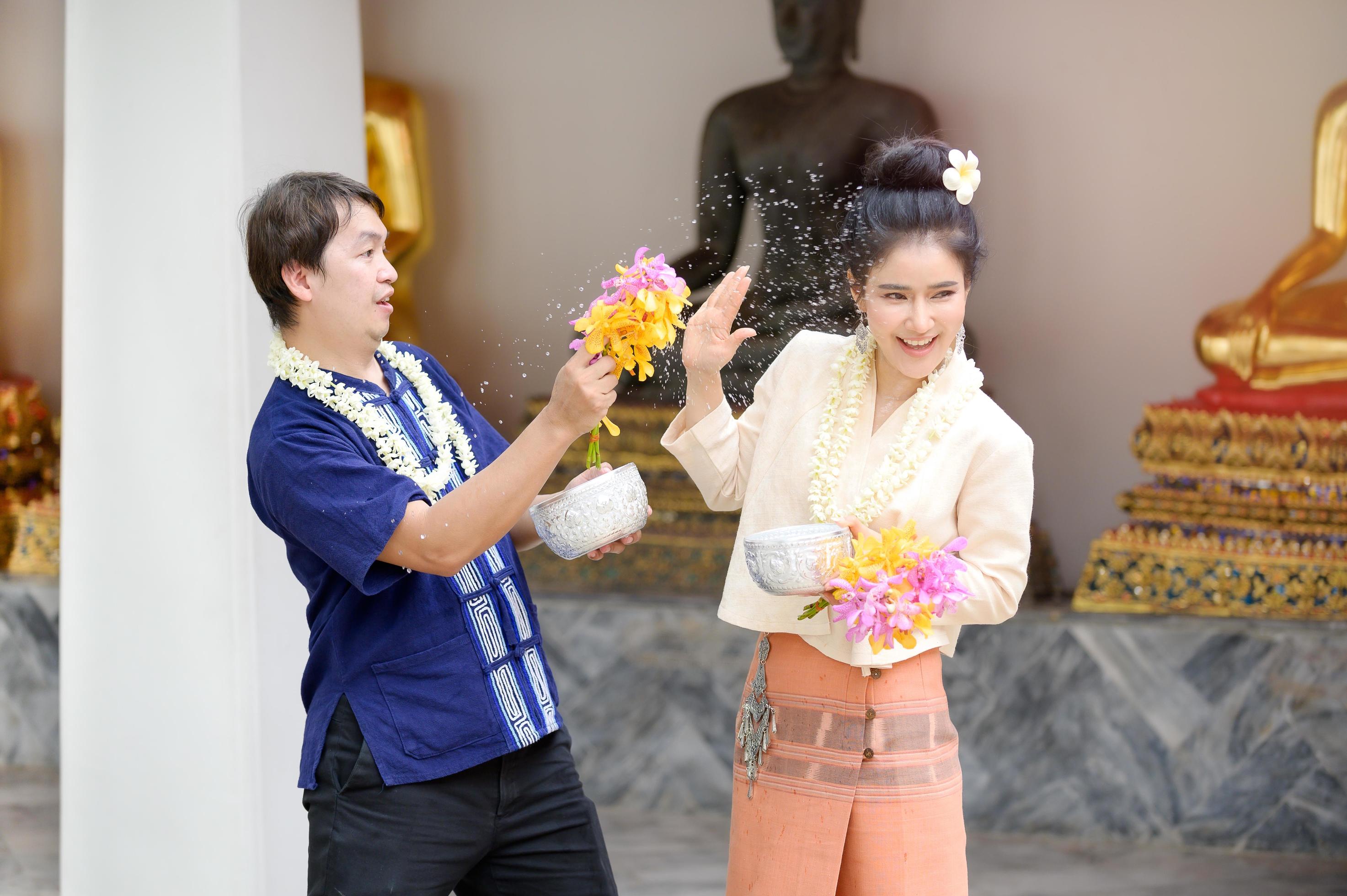 Young Thai men and women in traditional Thai dress hold flowers splashing water for fun at the Songkran water festival Stock Free