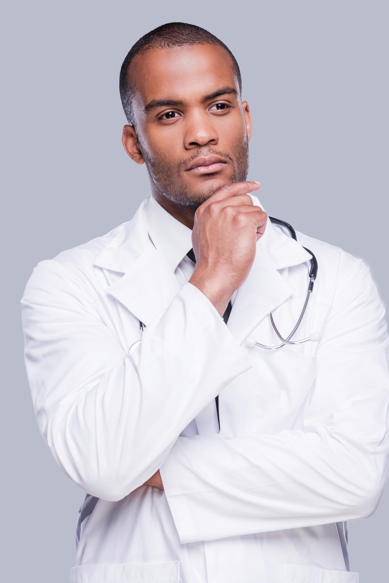 Pensive doctor. Thoughtful African doctor holding hand on chin and looking away while standing against grey background Stock Free