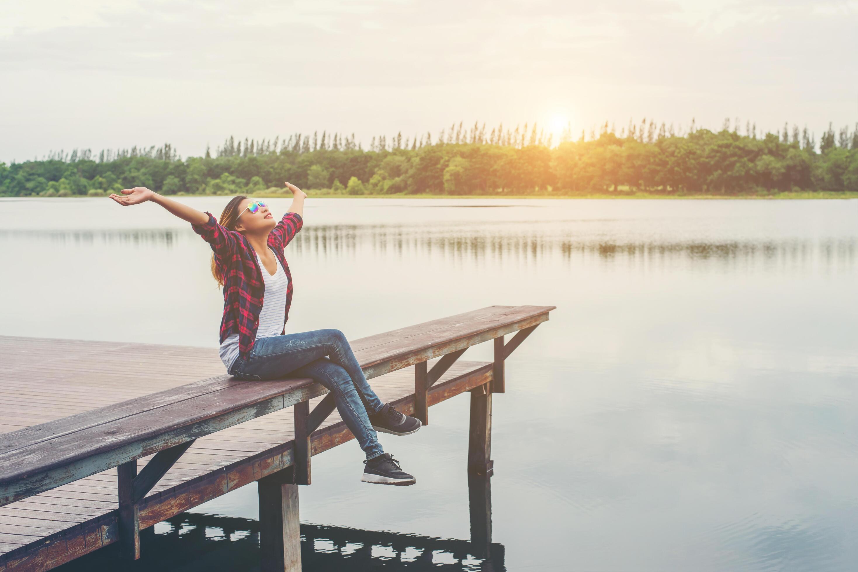 Young hipster woman sitting on pier raised hands,relaxing with natural freedom,enjoy and happy. Stock Free