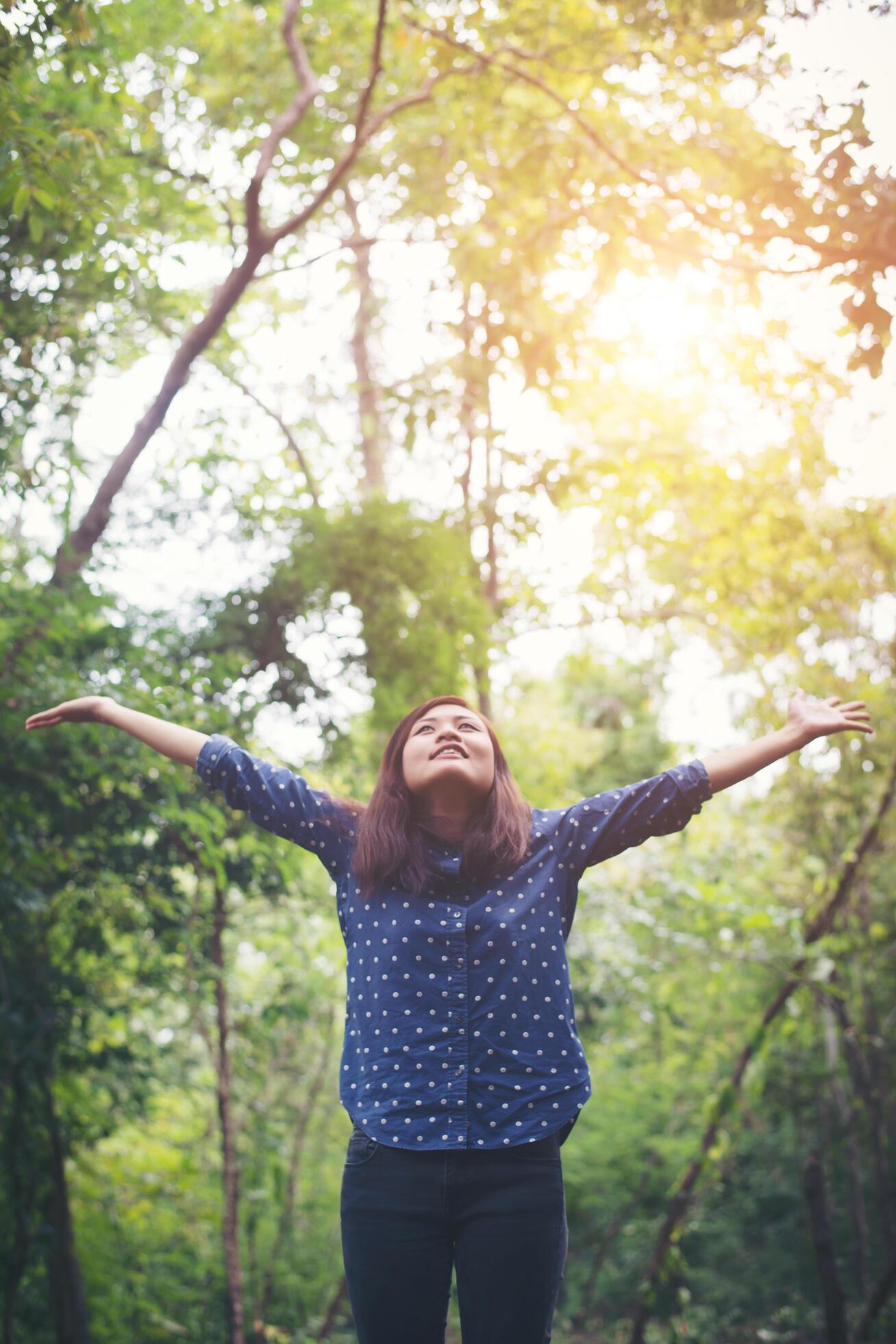 Attractive young woman standing in a forest, hands spread around and enjoy the refreshing natural surroundings. Stock Free