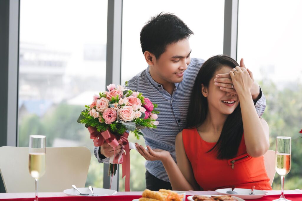 Lover with surpise flower bouquet at dinner table. Stock Free