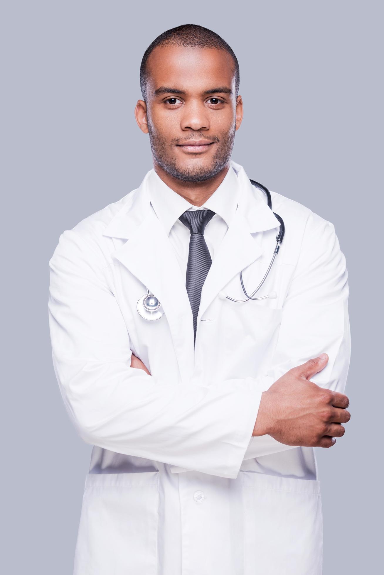 Confident male doctor. Confident African doctor looking at camera and keeping arms crossed while standing against grey background Stock Free