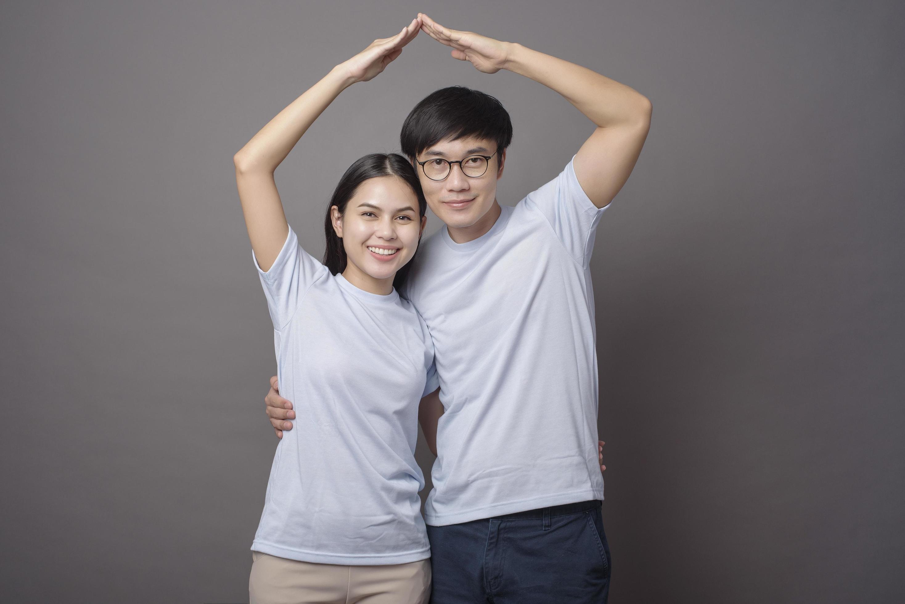 a happy couple wearing blue shirt is making armsroof in grey background studio Stock Free