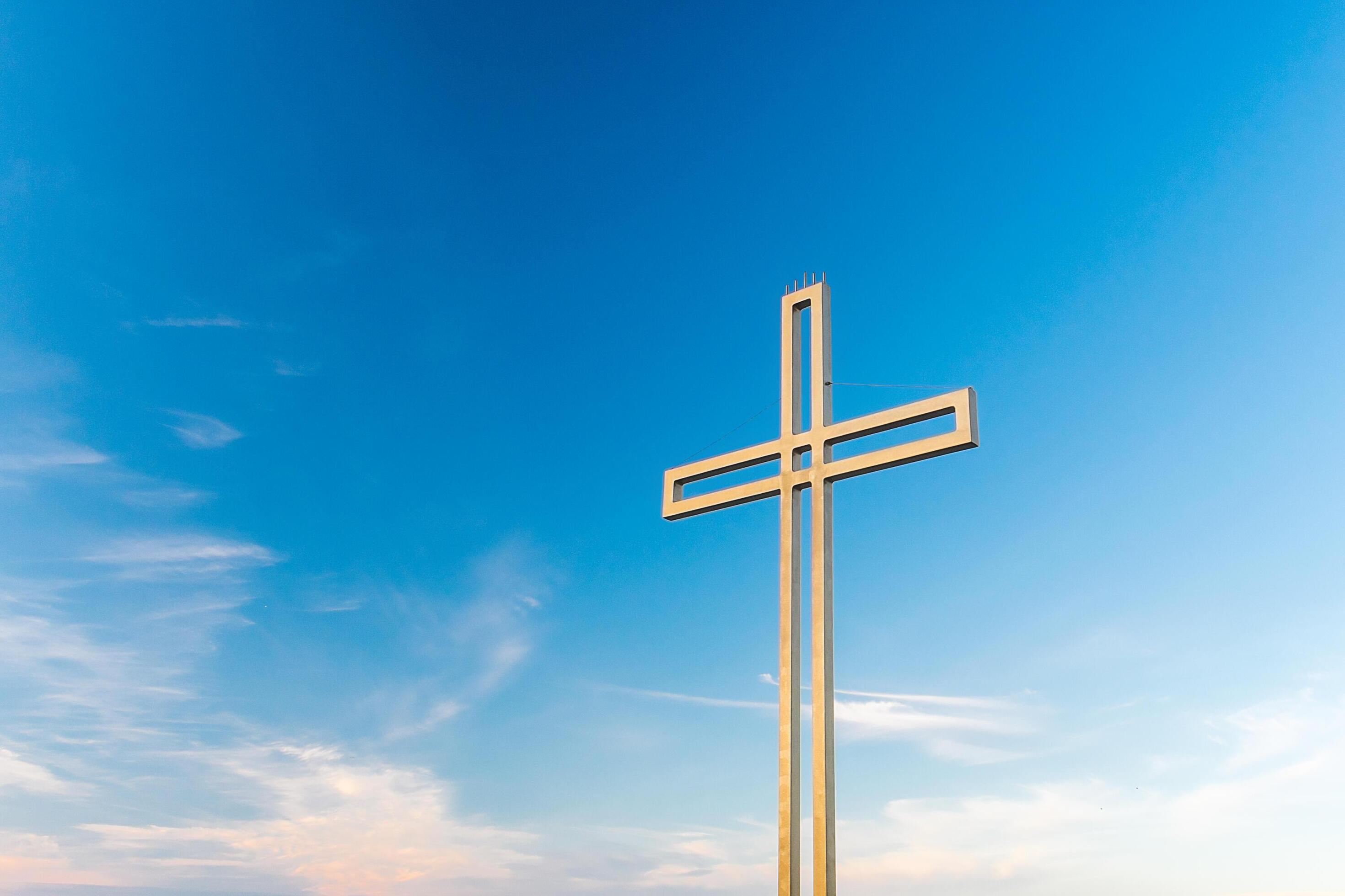 Golden cross against a background of blue sky with clouds. A minimalistic view of a gold-colored cross against the sky. Stock Free