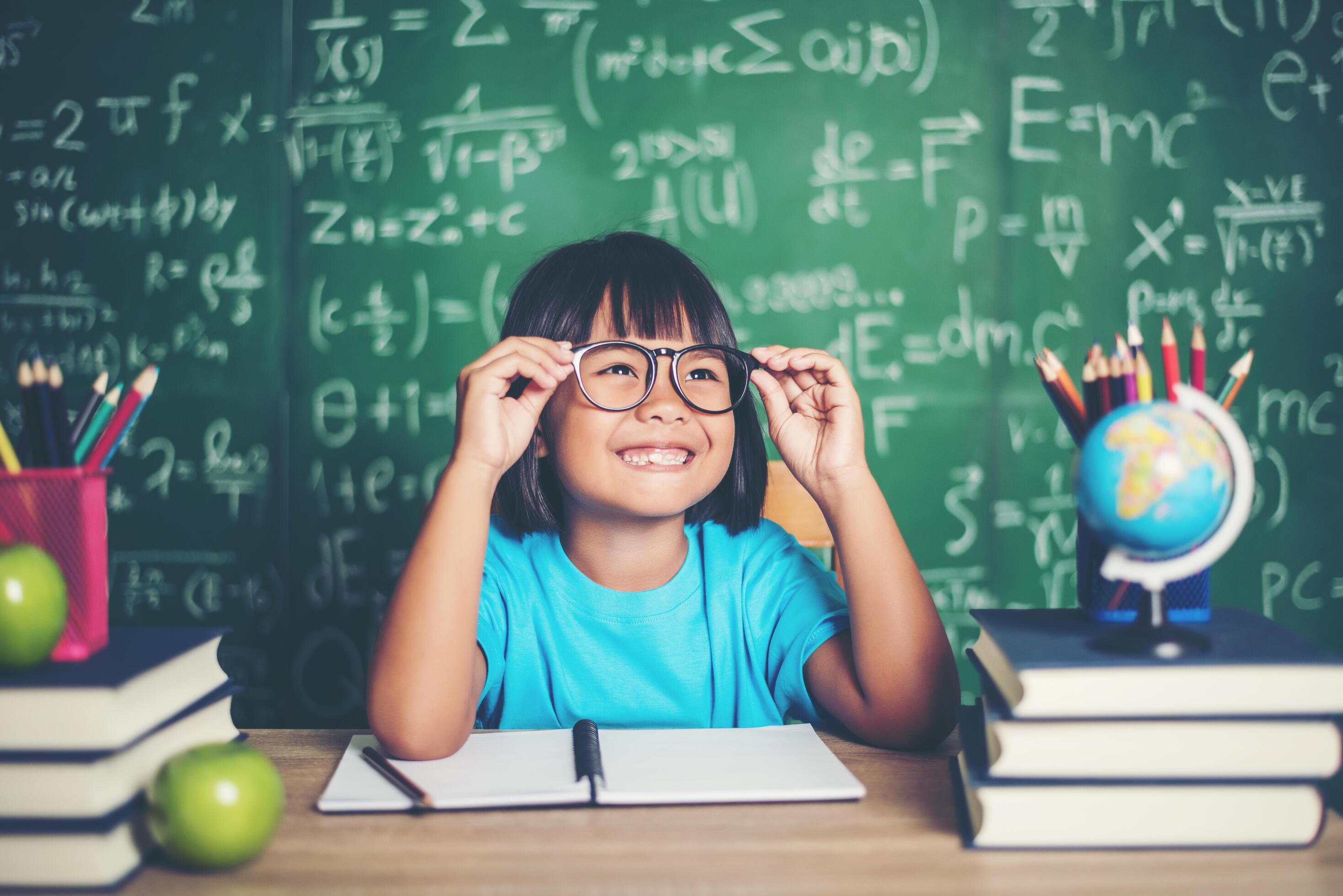 Thoughtful little girl with book near a school board Stock Free