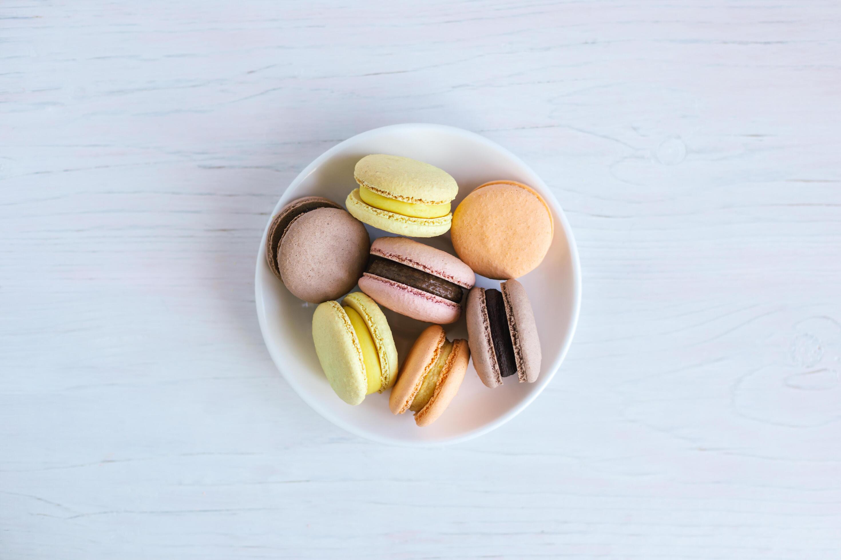 Tasty french macarons on a white plate. White wooden background, flat lay. Stock Free