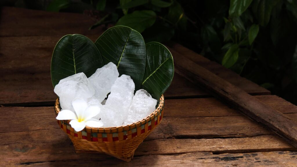 A basket filled with white alum crystals sits on a vibrant green shrub background. Stock Free