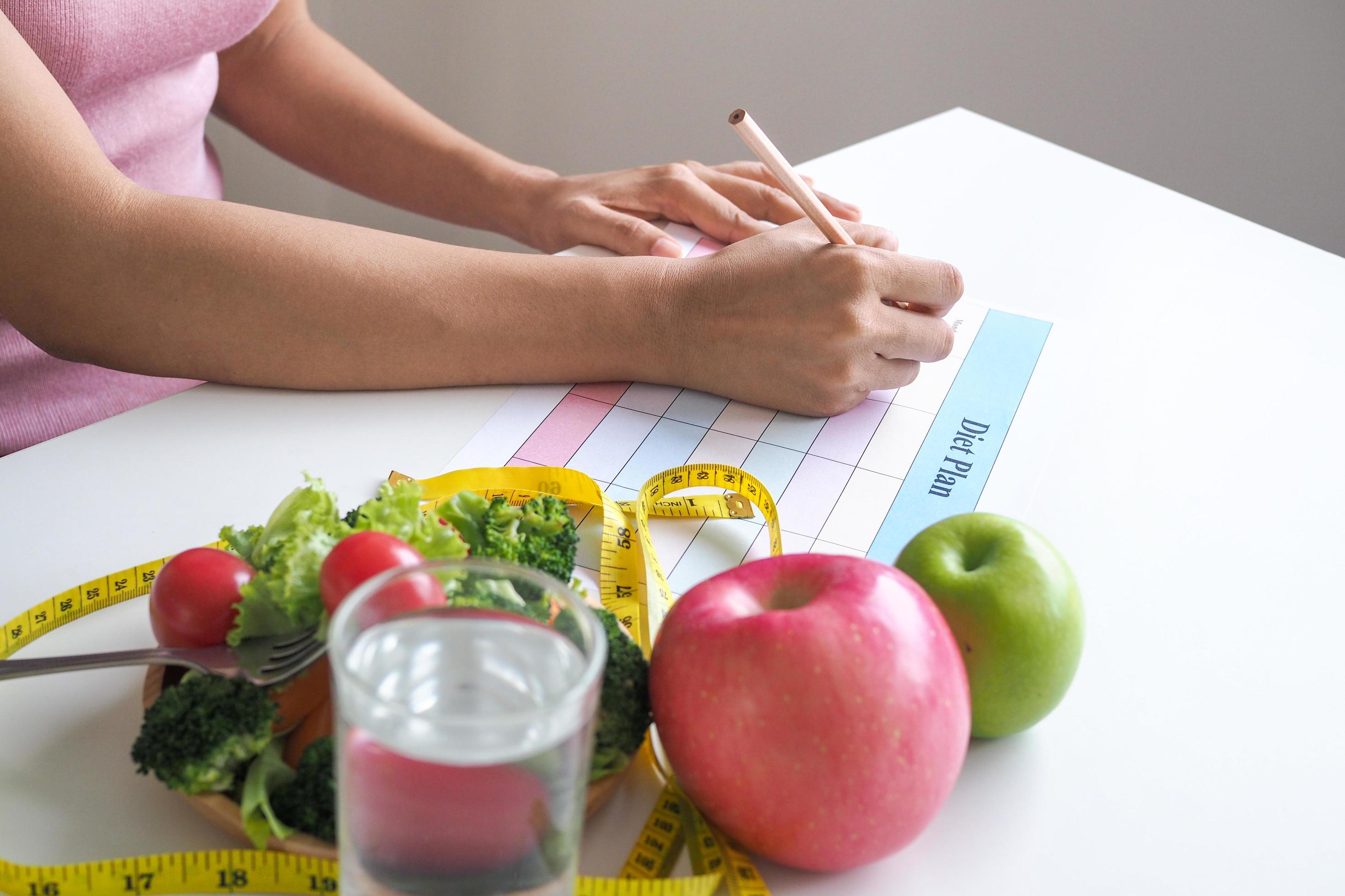 A girl sitting and writing a diet plan weight loss concept eat food that is good for the body. Such as fruits and vegetables. Stock Free