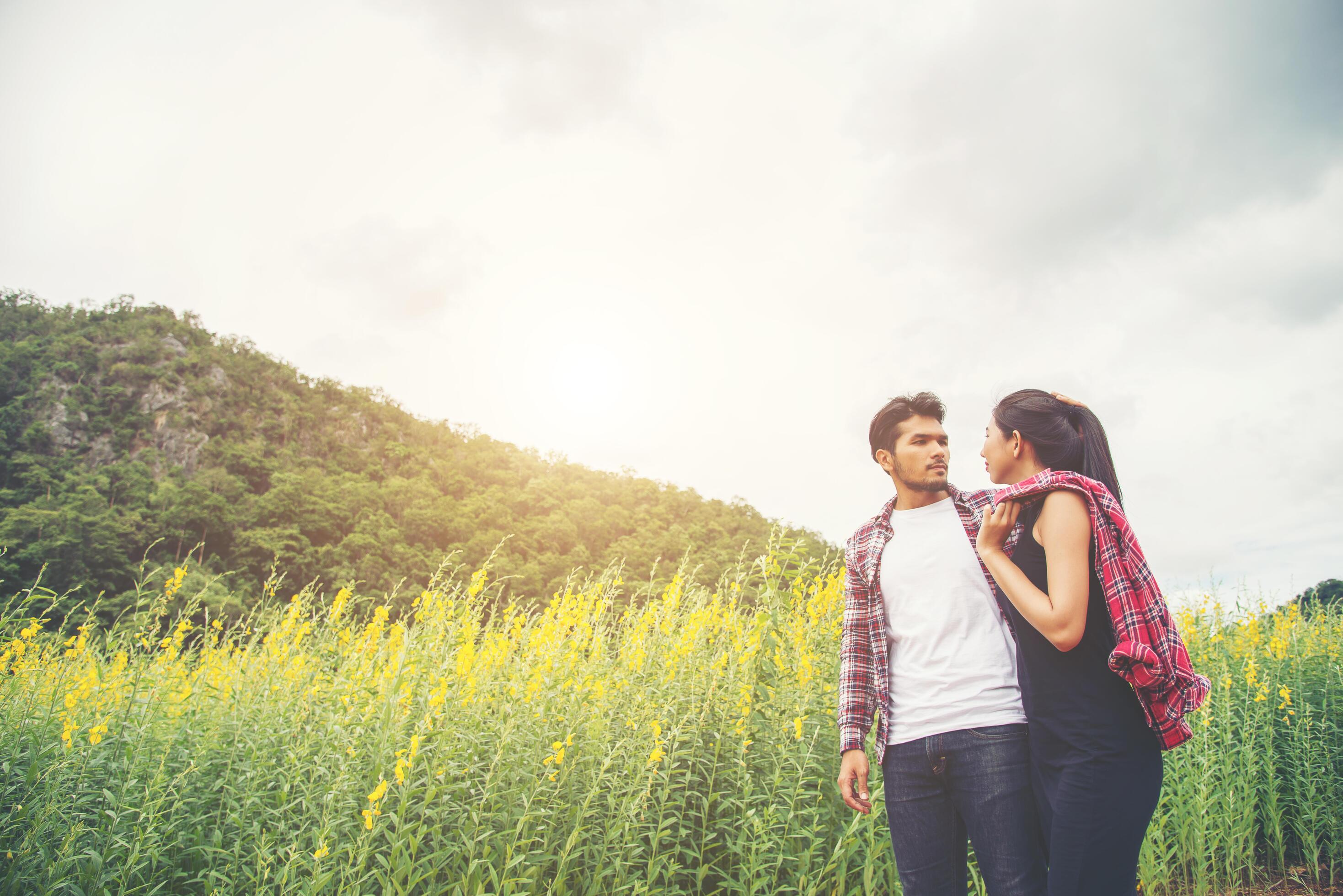 Young hipster couple relaxing in yellow flower field at summer. Stock Free