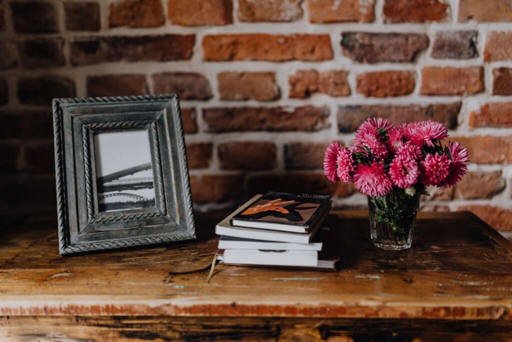 Photo frame, books and pink flowers in a vase on a wooden commode Stock Free