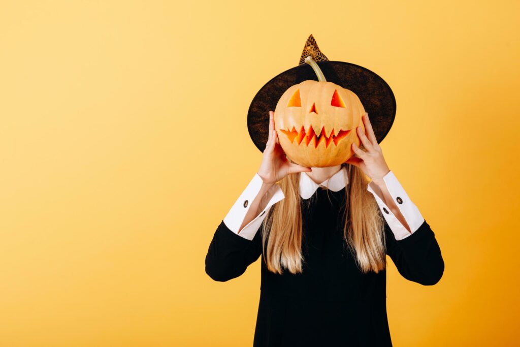 Woman standing against a yellow background holding pumpkin and hiding her face Stock Free