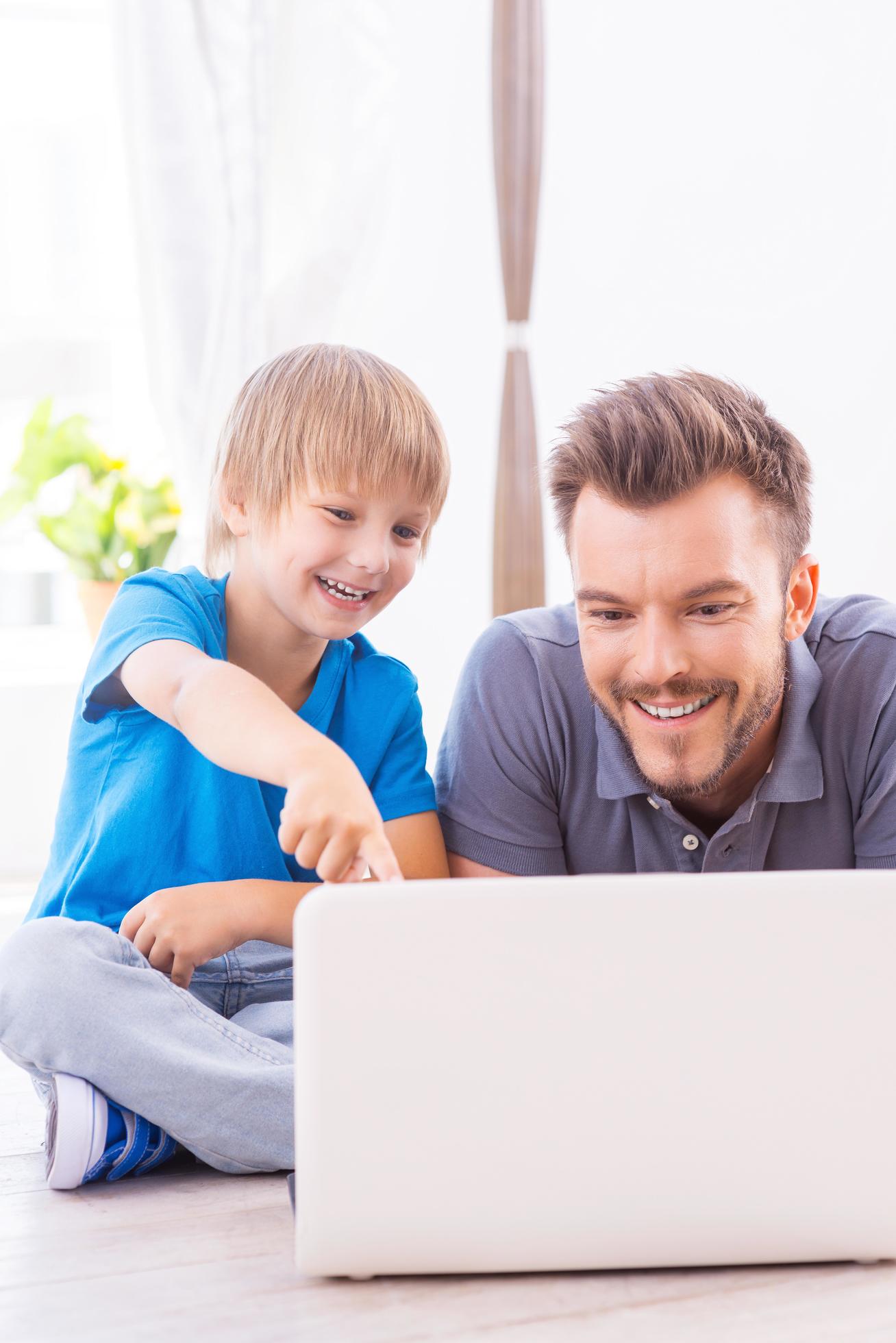 Spending time together. Happy father and son surfing the net at home while little boy pointing laptop monitor and smiling Stock Free