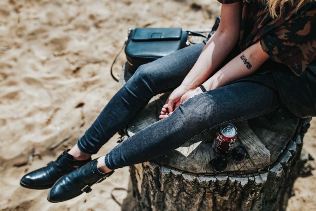 Beautiful blonde woman relaxing with a can of coke on a tree stump by the beach Stock Free