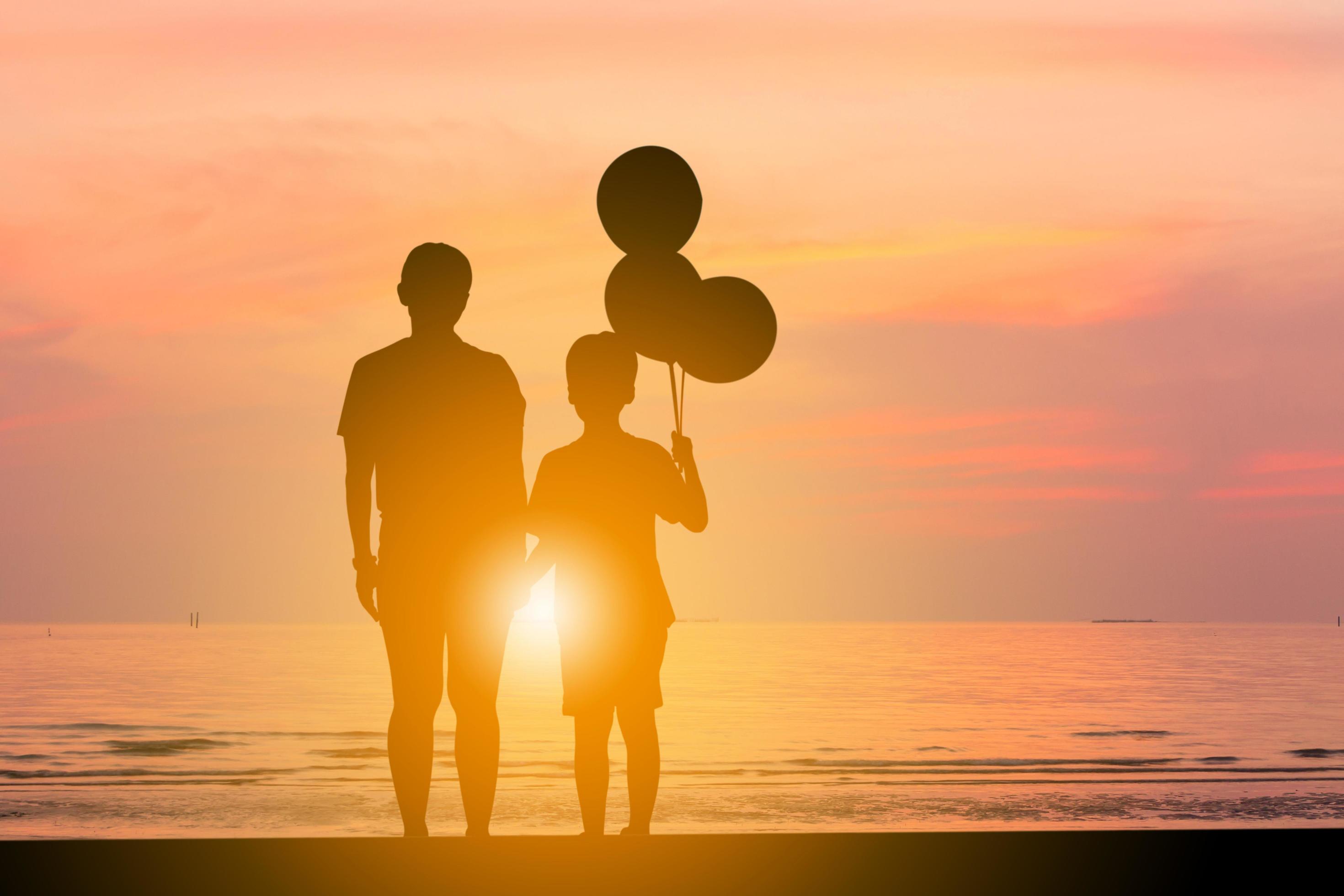 Silhouette of mother and son standing watching sunset on the beach with balloon in hand. Stock Free