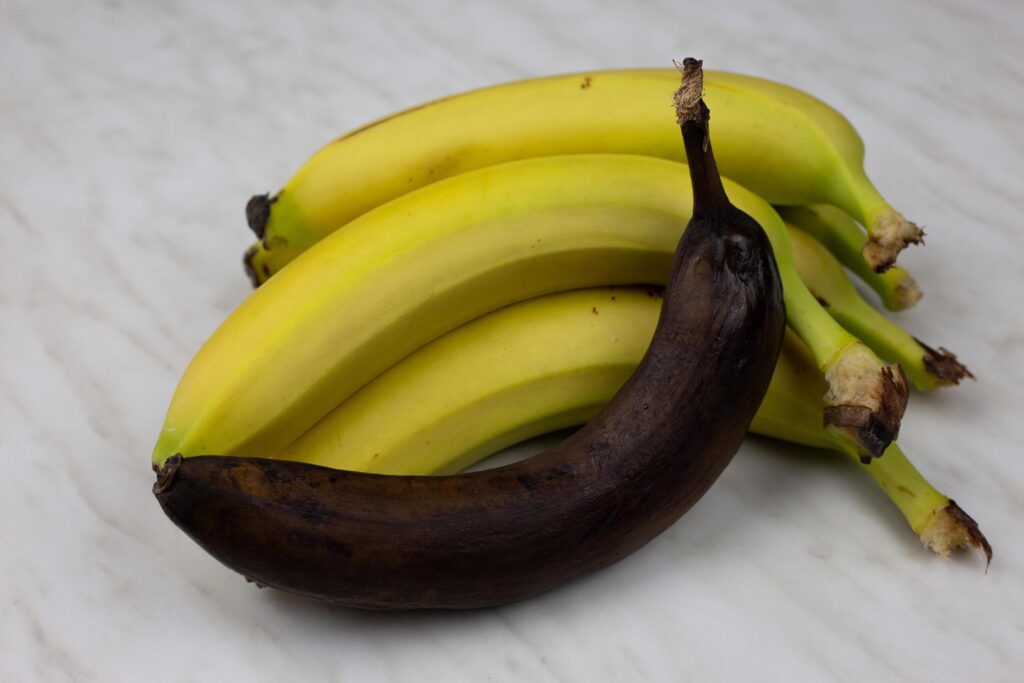 Rotten unpleasant banana in black peel against the background of juicy fresh banana fruit Stock Free