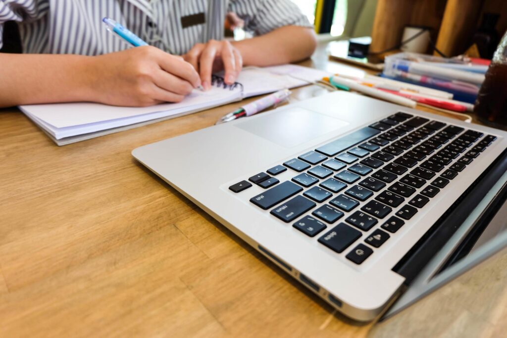 Young girl student is writing notebook and using laptop, learning and education concept Stock Free