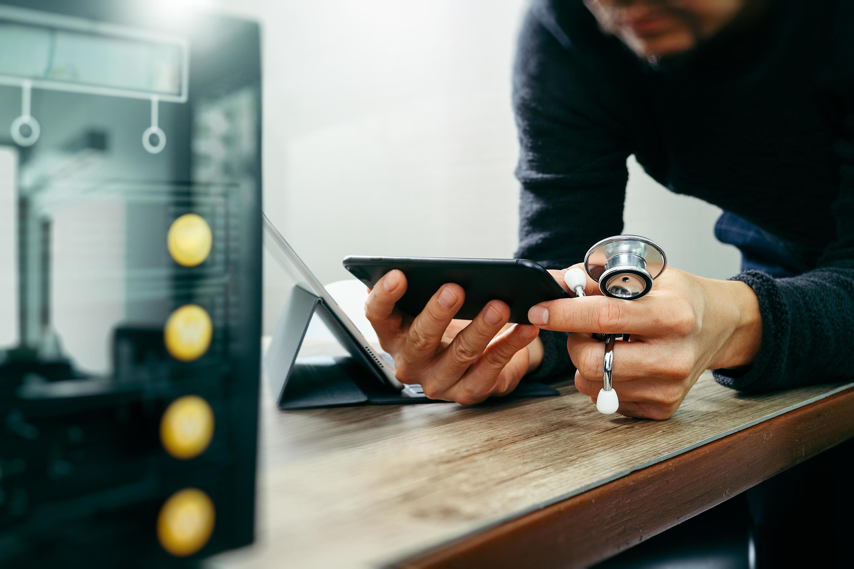 medical doctor hand working with smart phone,digital tablet computer,holding stethoscope,compact server on wood desk Stock Free