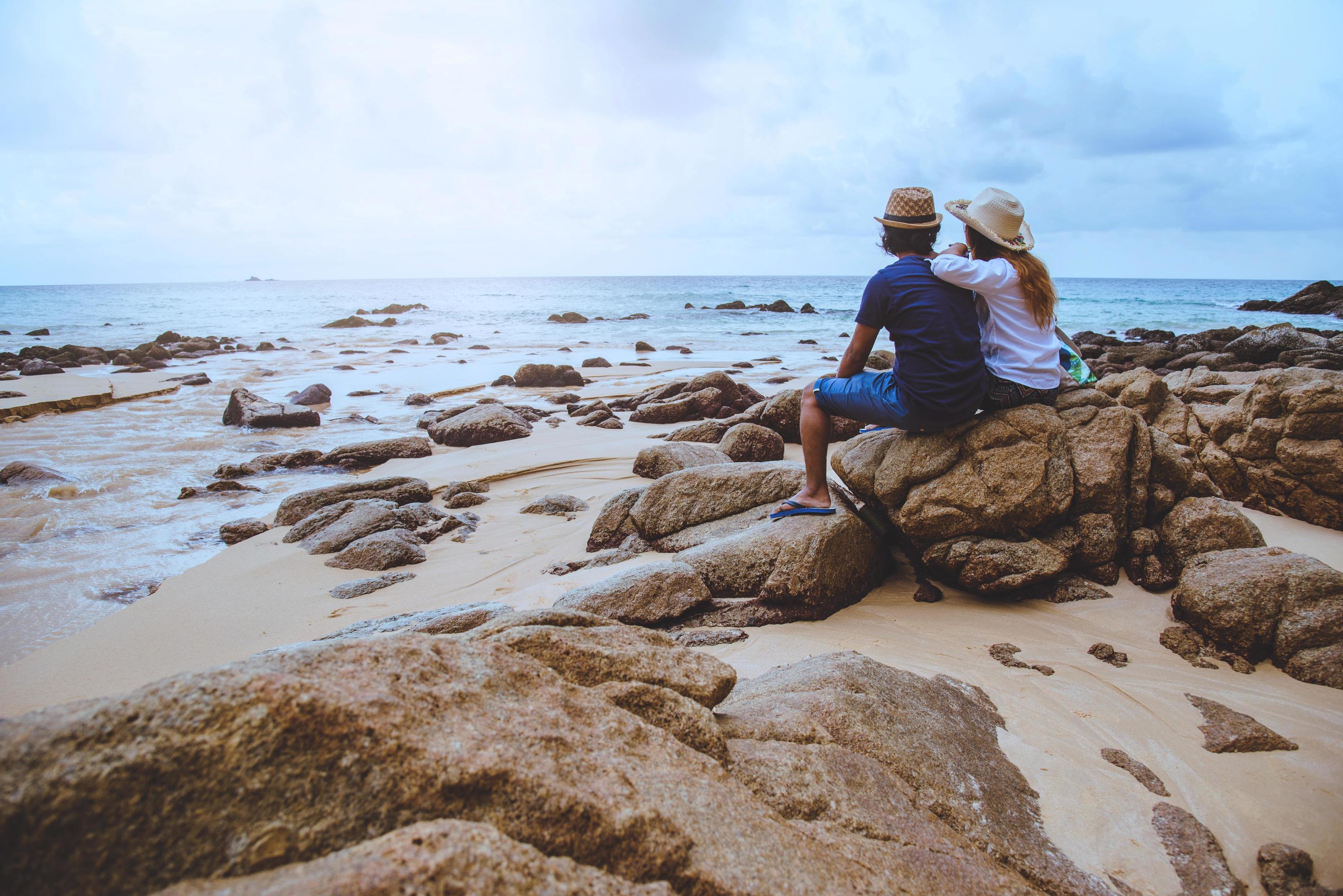 Asian lovers happy on the beach.The sky is bright Travel nature and sitting relax on the rocks at the sea at phuket. in Thailand. summer. Stock Free