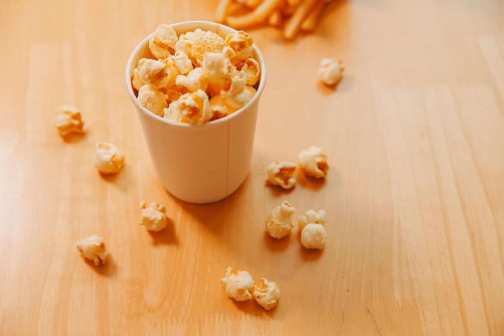 A bucket of popcorn, top-view, warm colors, light brown wooden background, flat lay, daylight macro close-up Stock Free