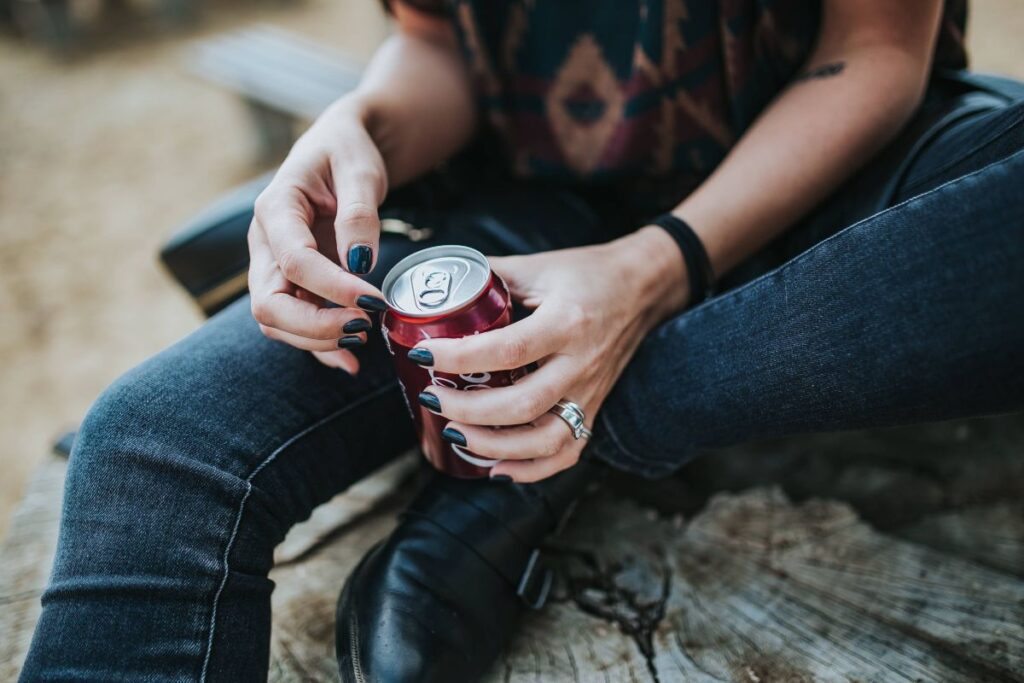 Beautiful blonde woman relaxing with a can of coke on a tree stump by the beach Stock Free