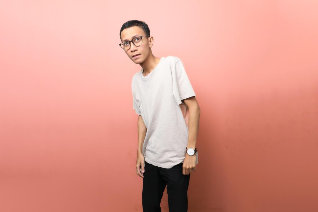 an Asian man wearing a plain white t-shirt with glasses with a surprised face isolated on red background Stock Free