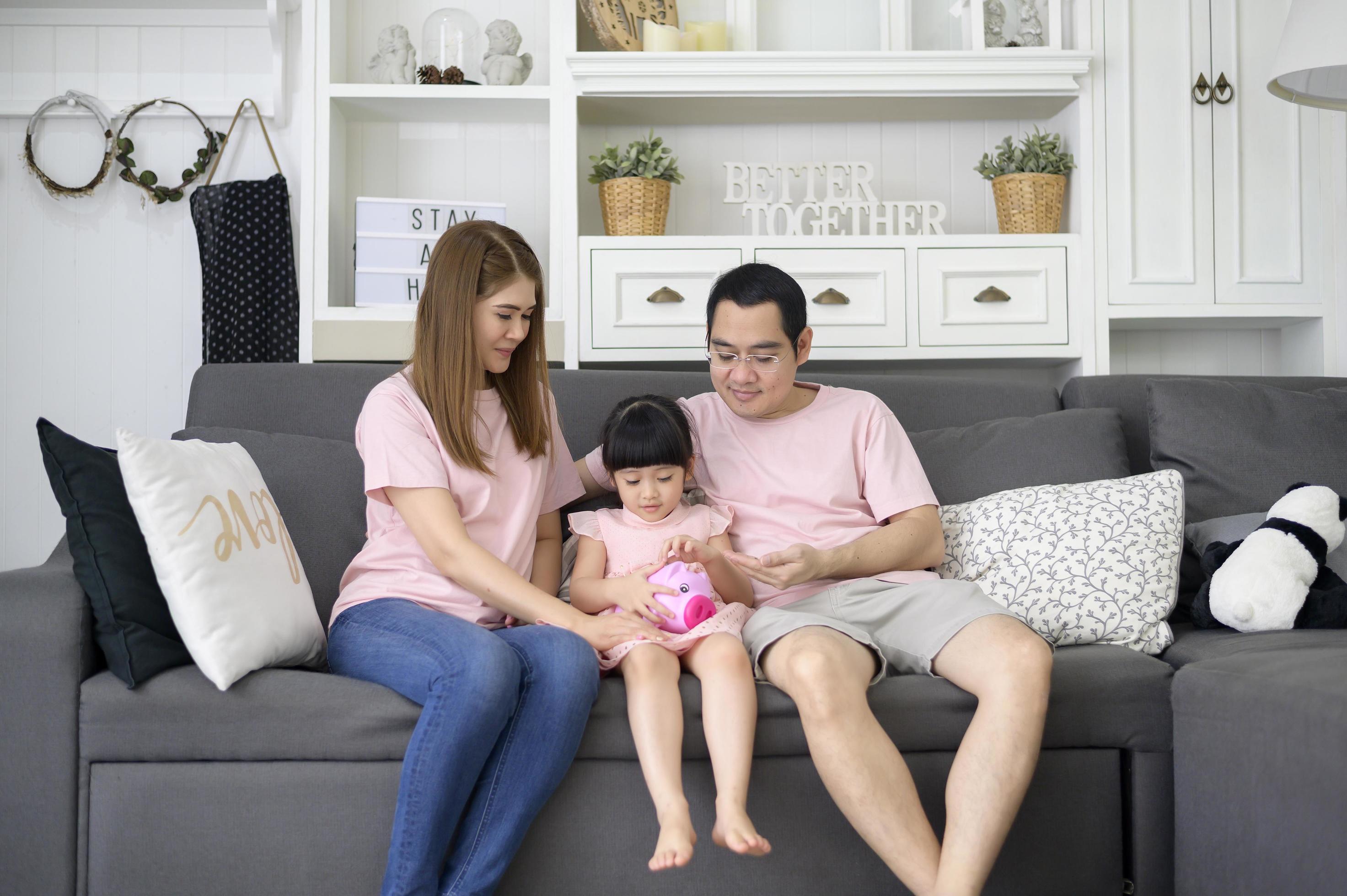 An asian family is teaching daughter on savings money with a piggy bank, financial planning concept Stock Free