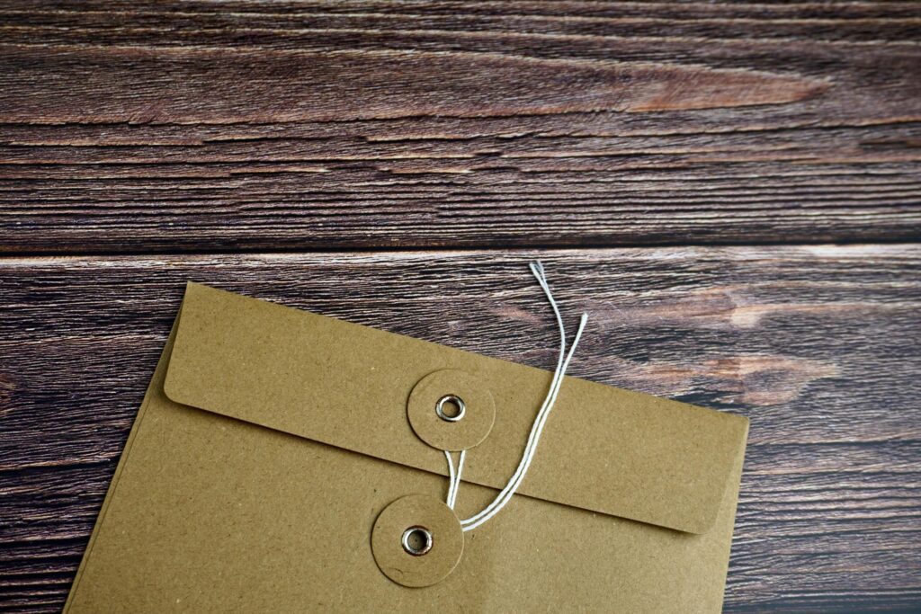 Cropped brown envelope with opened thread lock position isolated on horizontal ratio brown surface table background. Stock Free