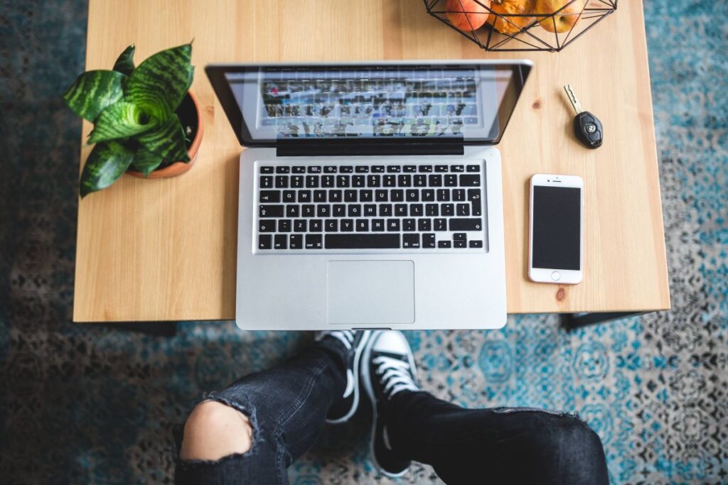 Woman in ripped jeans and black sneakers with a silver laptop on a wooden table Stock Free