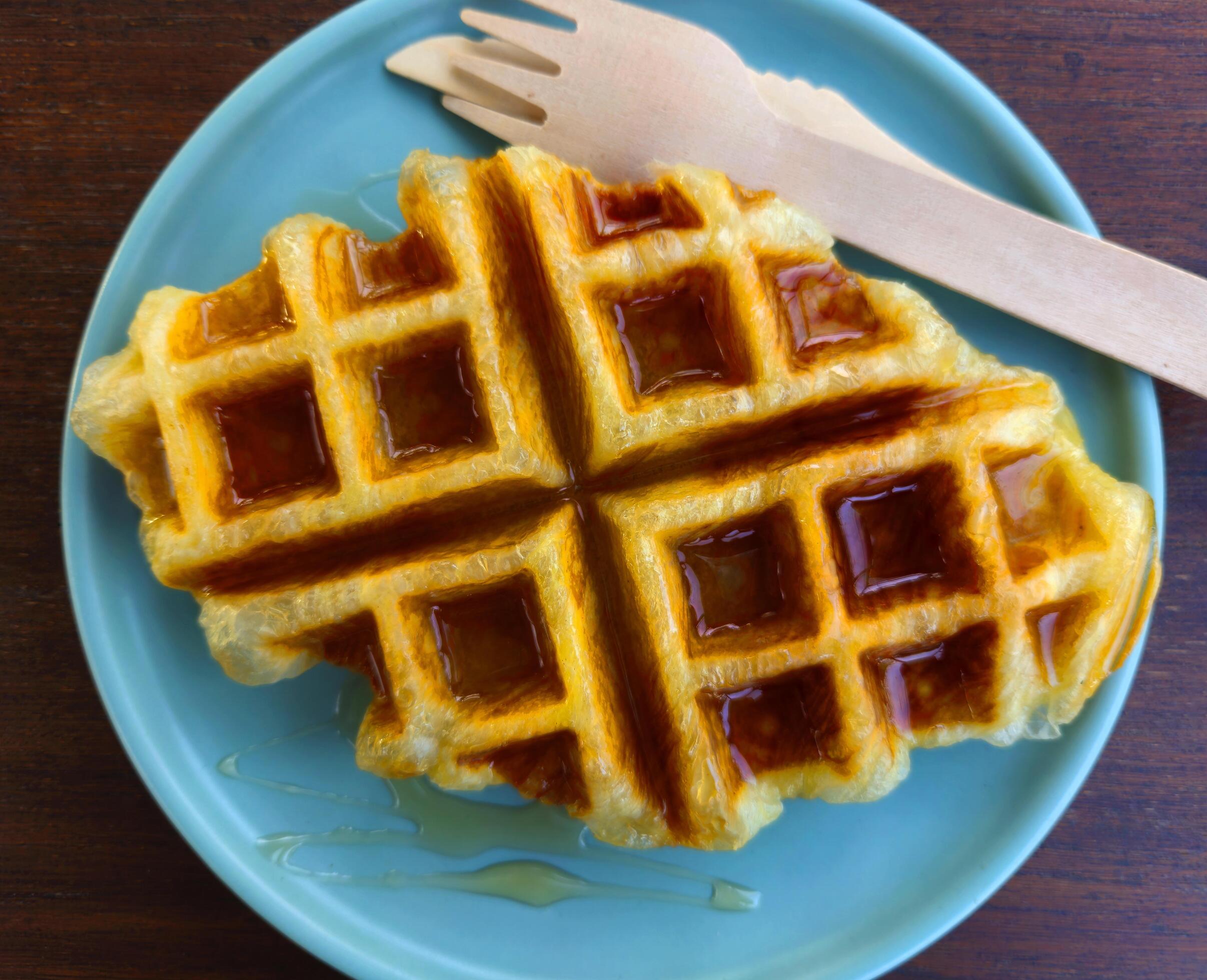 Closeup waffle topped with honey sauce on blue plate at cafe. Sweet bakery in dish on wooden table or background with copy space. Stock Free