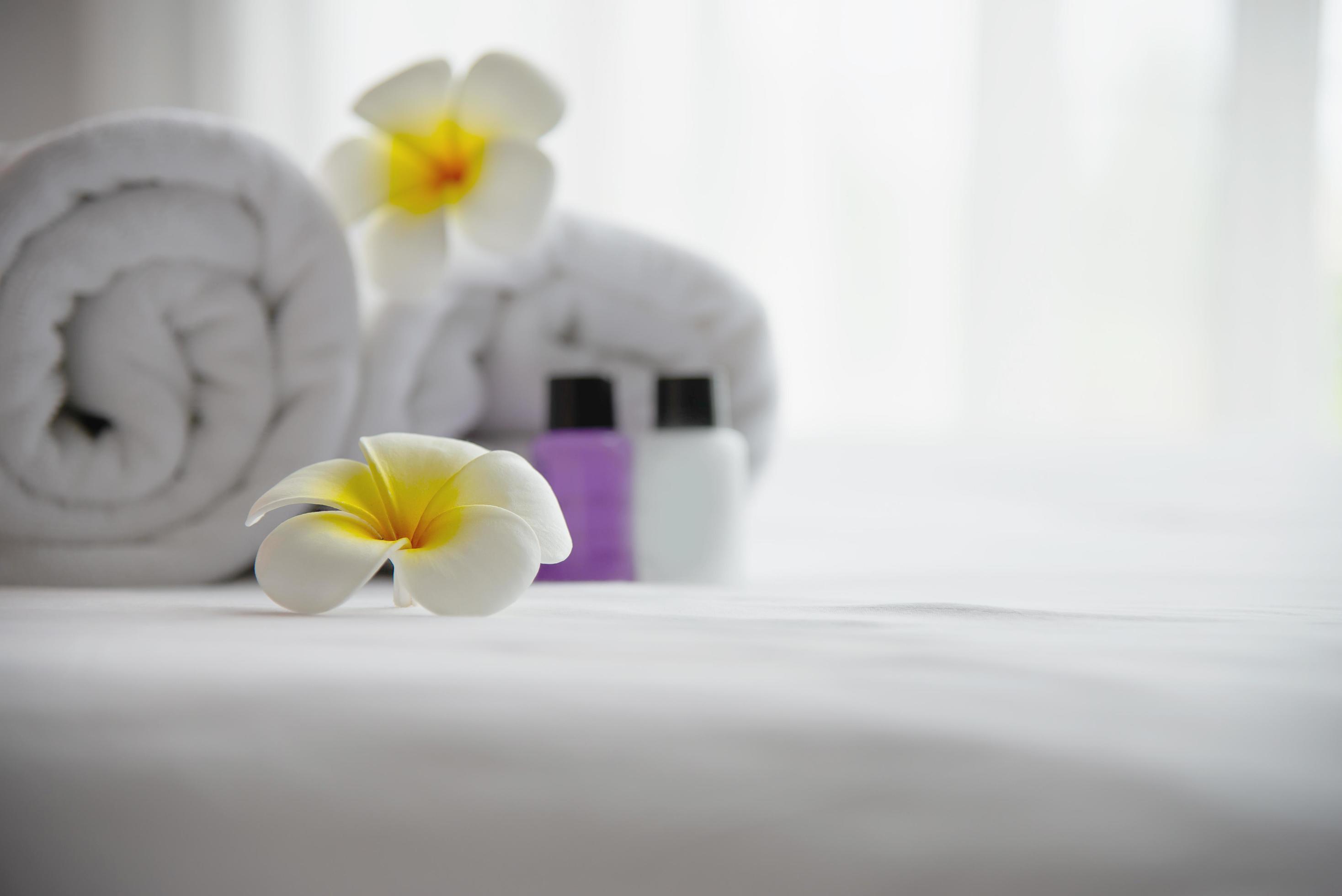 Hotel towel and shampoo and soap bath bottle set on white bed with plumeria flower decorated – relax vacation at the hotel resort concept Stock Free