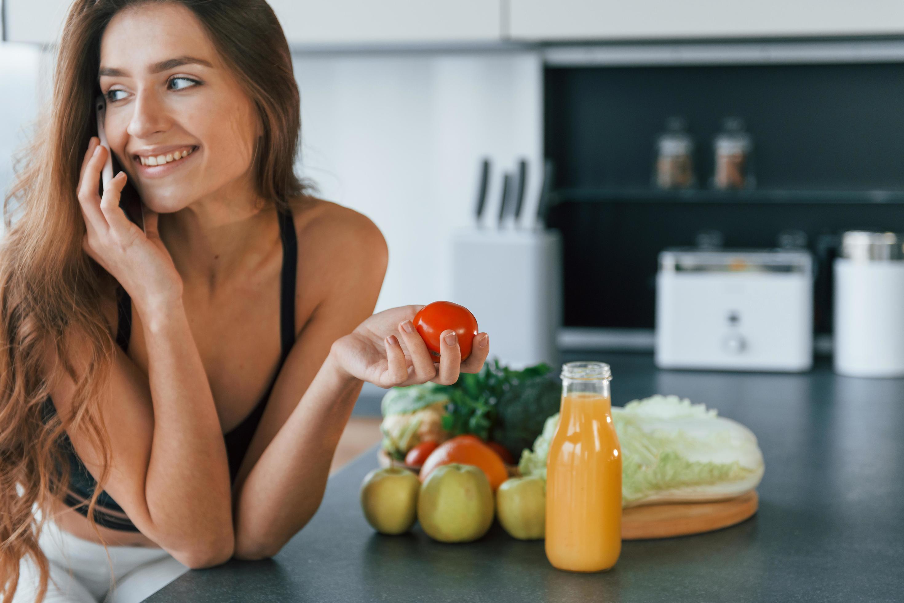 Talks by the phone. Young european woman is indoors at kitchen indoors with healthy food Stock Free