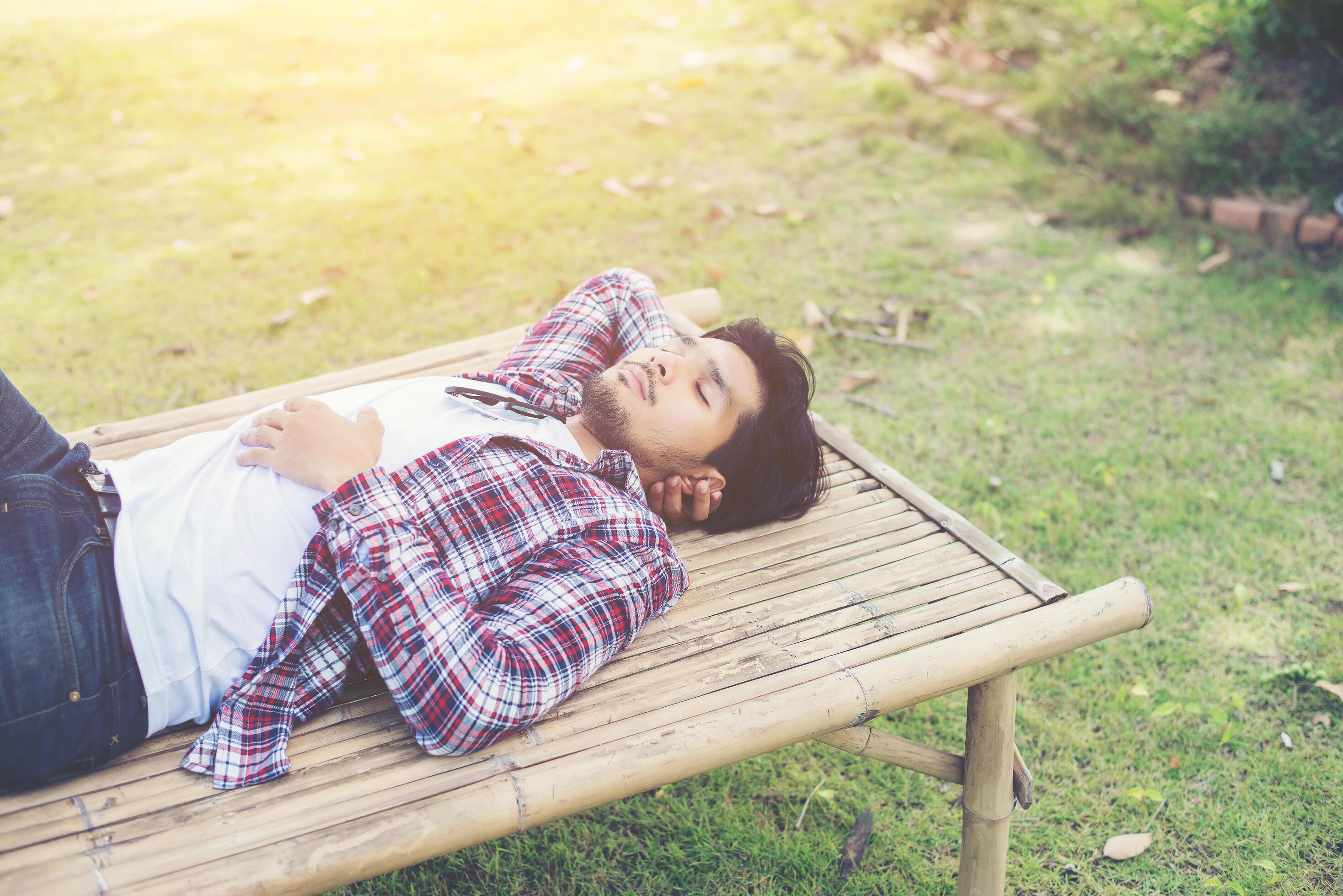 Happy young hipster lying on bench in the nature park. Stock Free