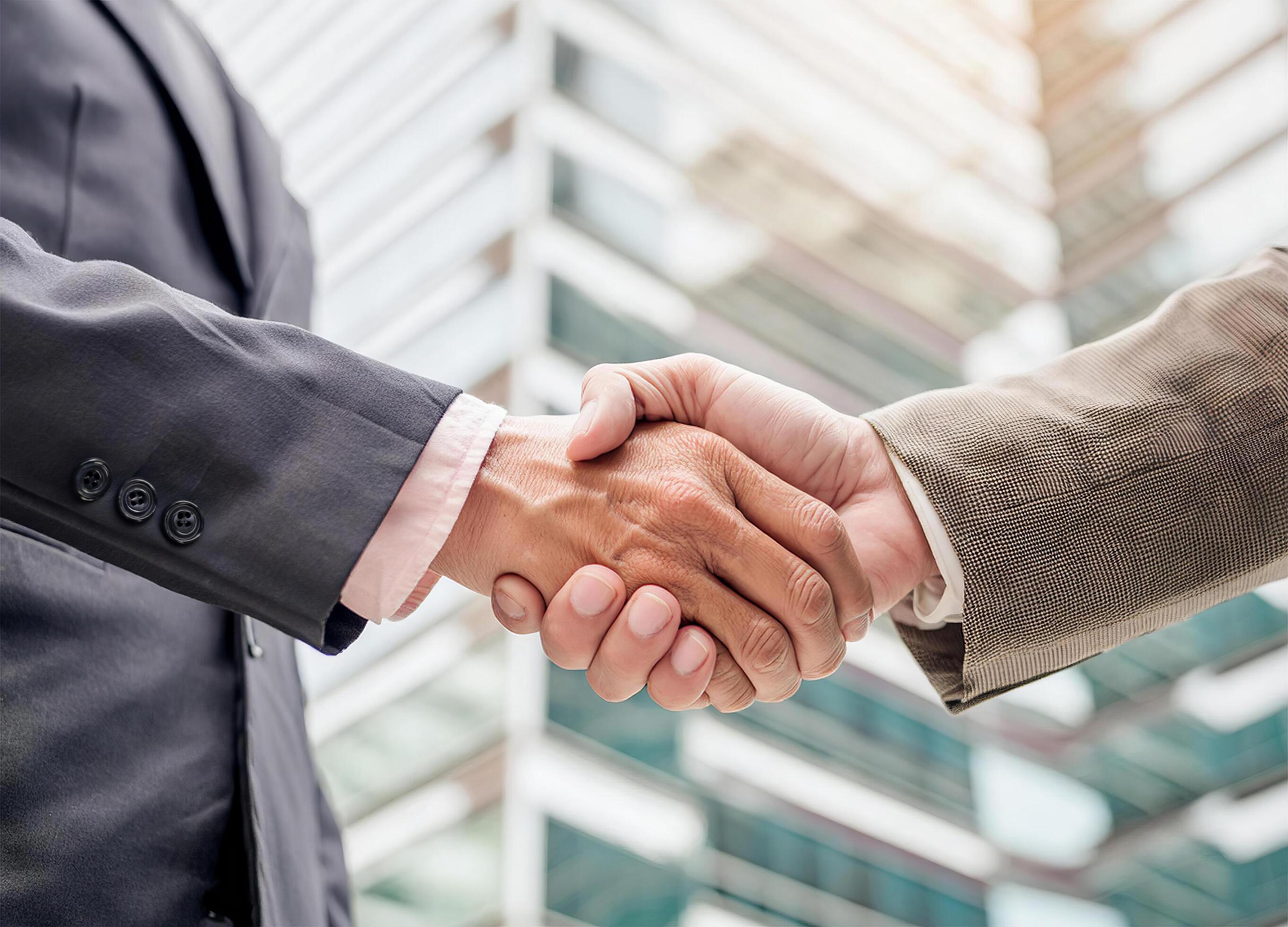 Close up of hand of Two business people shaking hands,blurred building background Stock Free