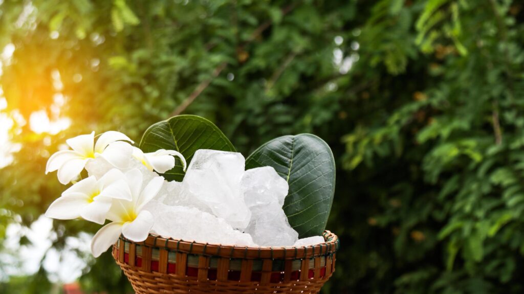 A basket filled with white alum crystals sits on a vibrant green shrub background. Stock Free