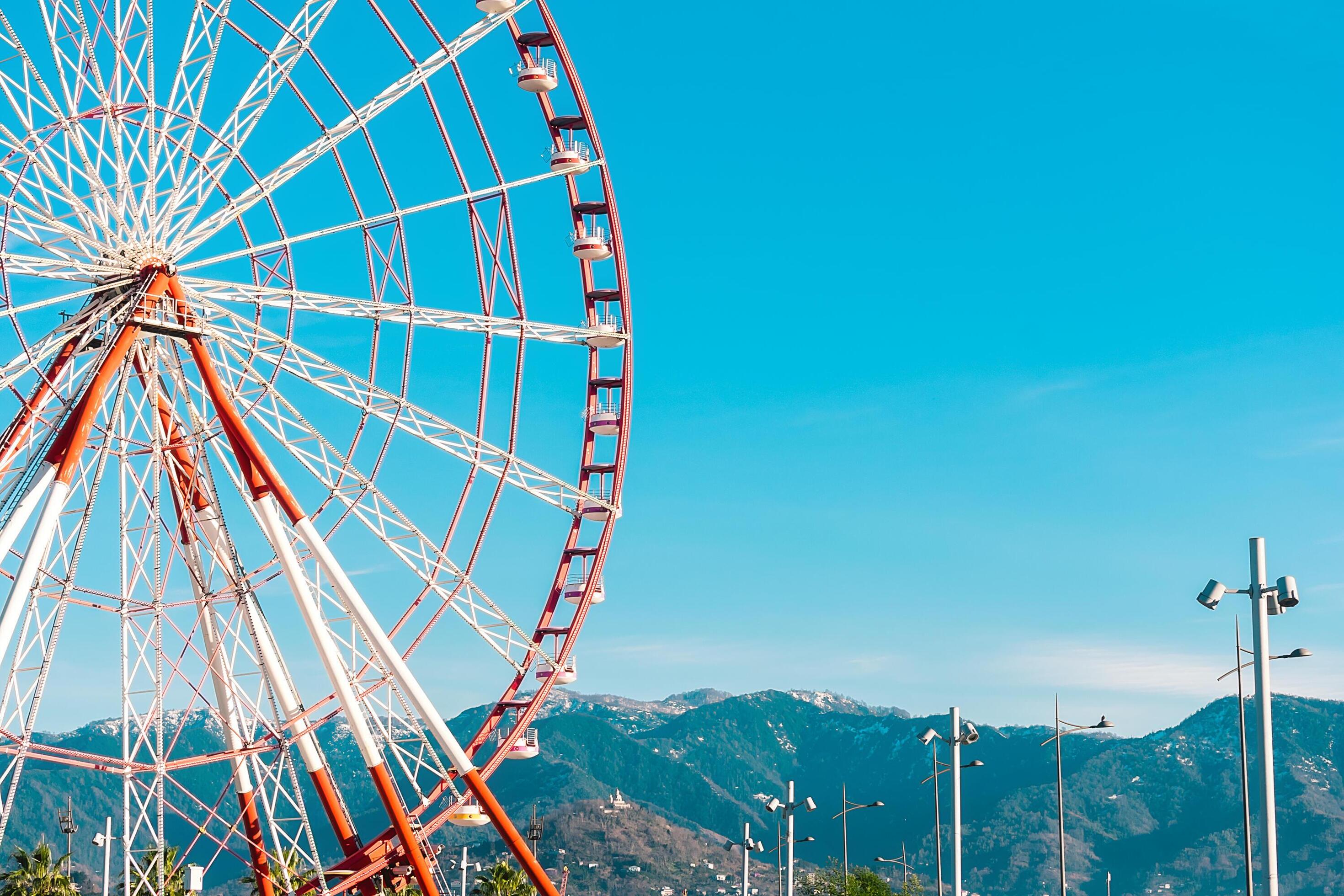 View of the Ferris wheel attraction against a background of blue sky between palm trees. Ferris wheel in the Georgian city of Batumi. Stock Free