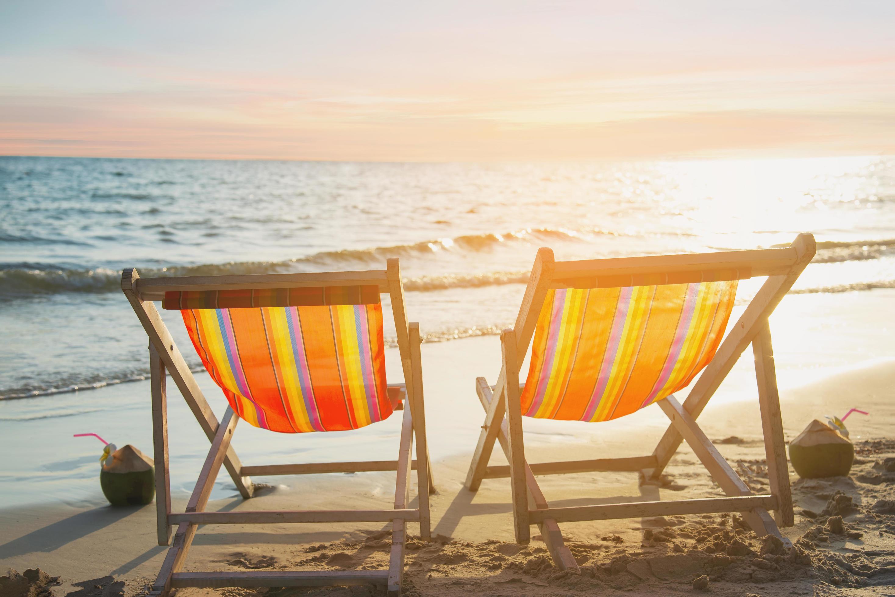 Couple relax chair on sand beach with warm sunset – vacation in beautiful sea nature concept Stock Free