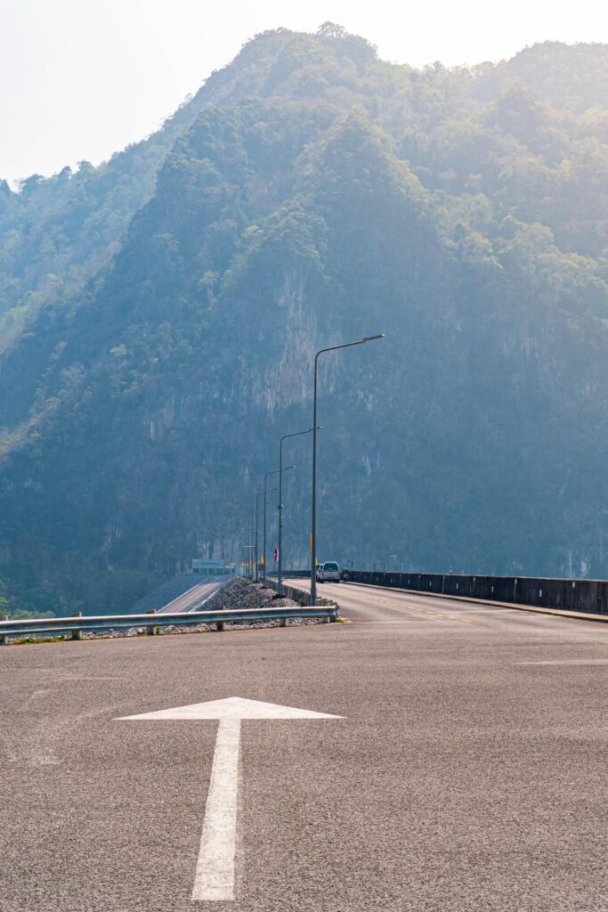 The scene of the road at the top of the dam, with the mountains in the background and a light pole. Stock Free