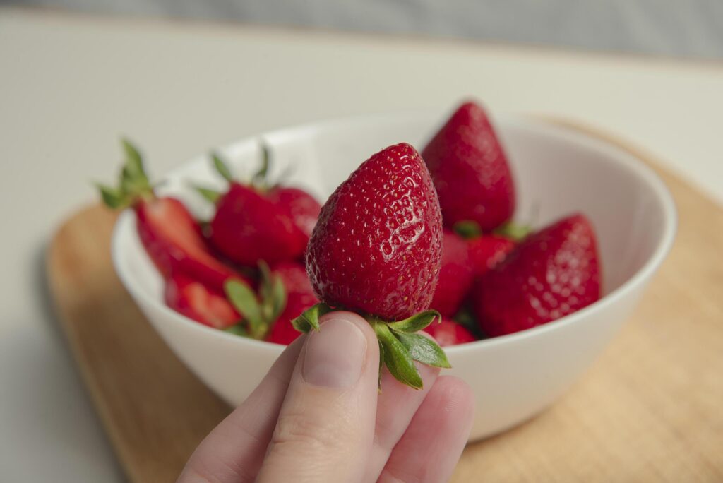 Close-up of strawberries in a woman hands against the background of strawberries in a bowl Stock Free