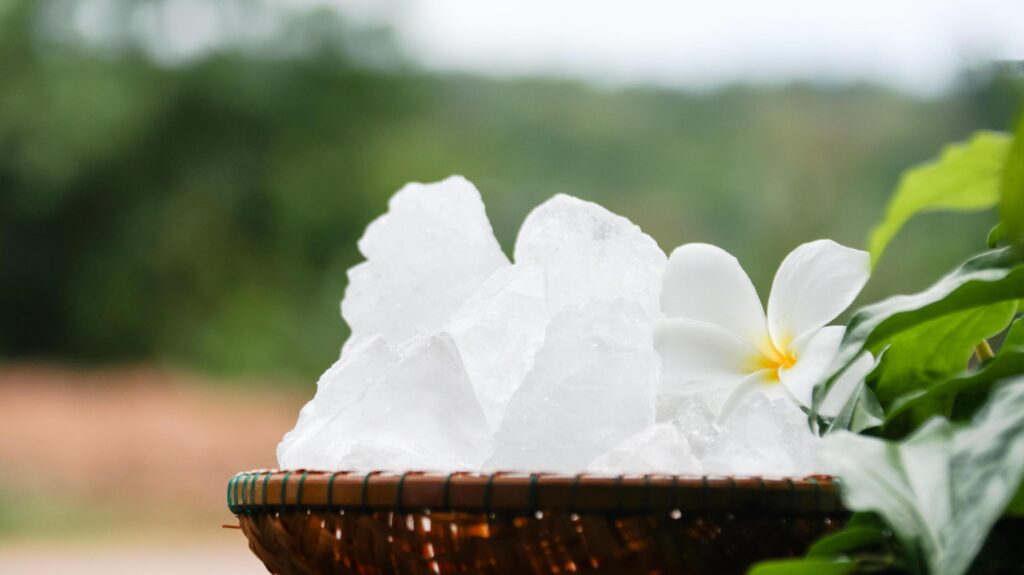 A basket filled with white alum crystals sits on a vibrant green shrub background. Stock Free