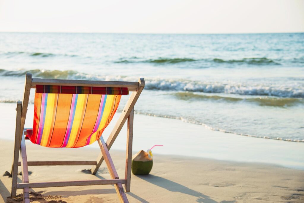 Relax beach chair with coconut pineapple and cocktail glass on clean sand beach with blue sea and clear sky – sea nature background relax concept Stock Free