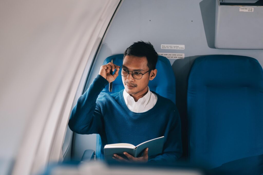 Handsome young Asian businessman or male executive manager reading a book during the flight for his business trip. Airplane or private jet concept Stock Free