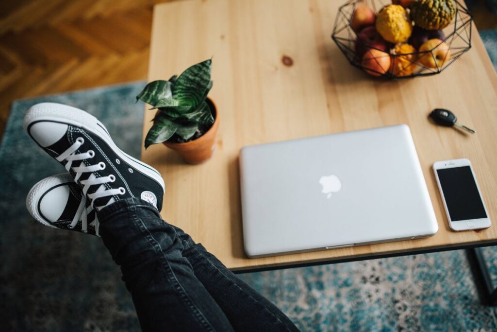 Woman in ripped jeans and black sneakers with a silver laptop on a wooden table Stock Free