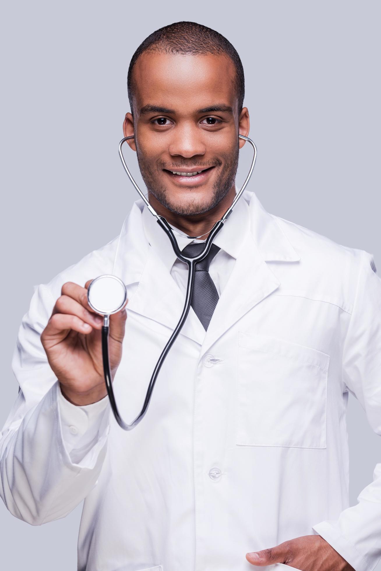 Medical exam. Confident African doctor stretching out his stethoscope and smiling while standing against grey background Stock Free